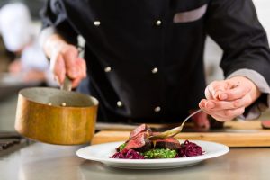 A chef pouring sauce onto a steak.